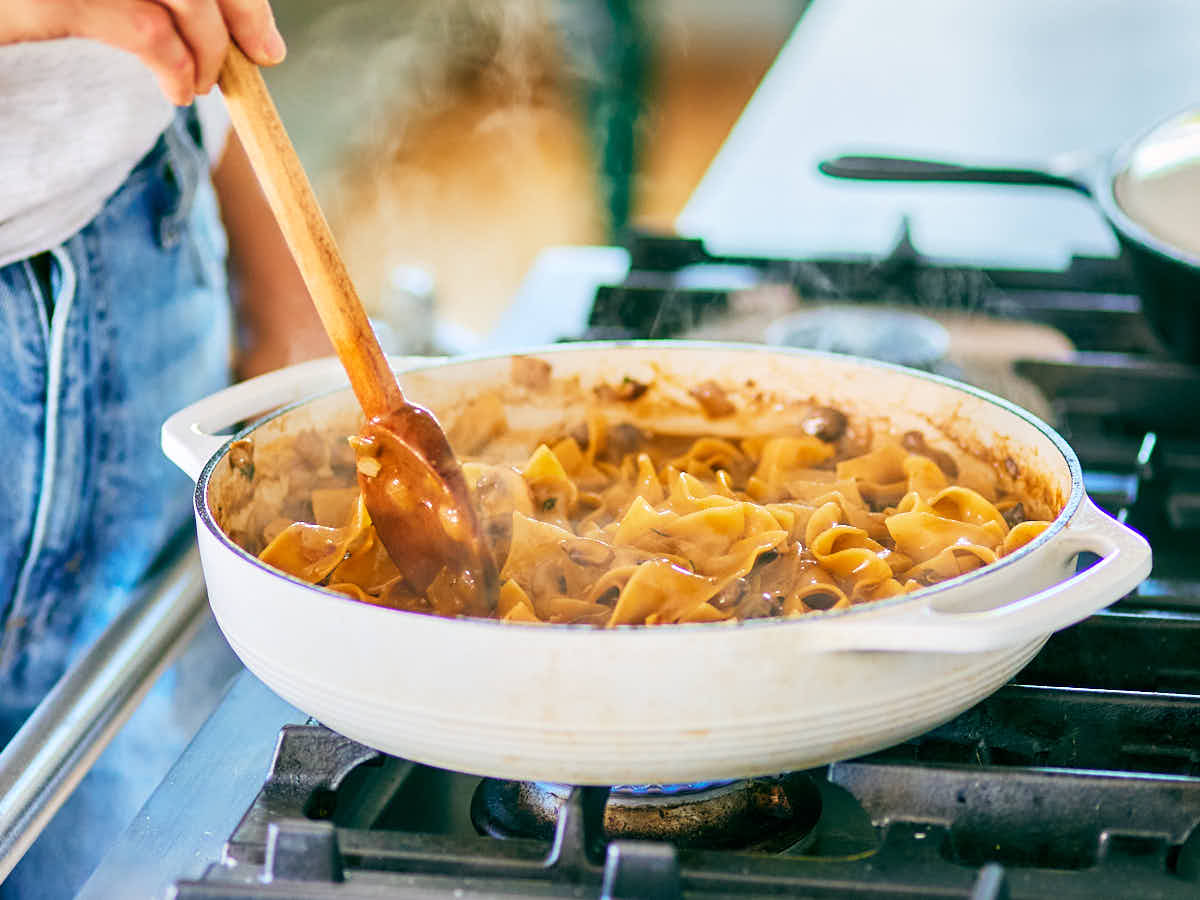A woman stirring one pot mushroom stroganoff on the stove with a wooden spoon.