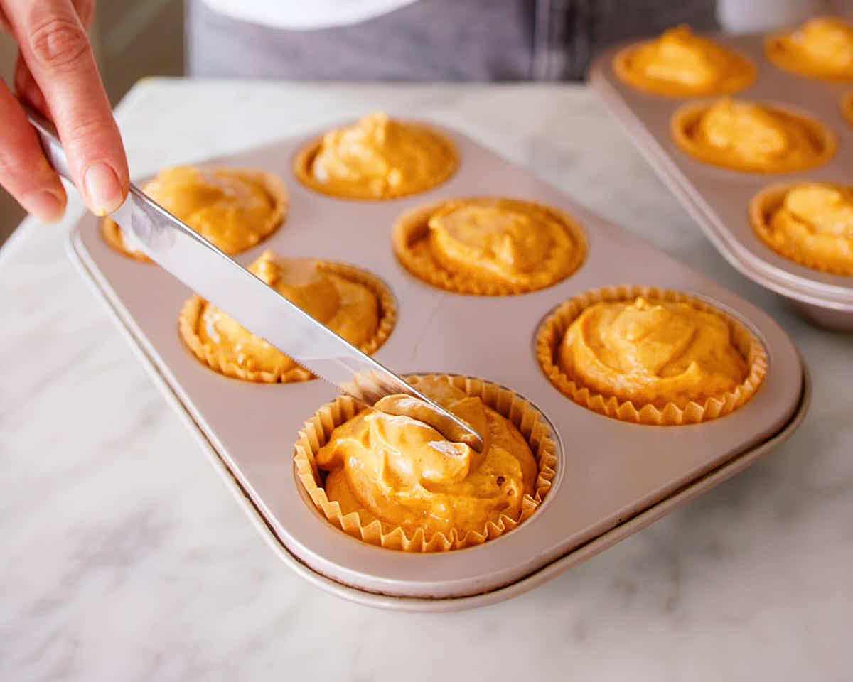 A knife pressing into the top of muffin batter before baking to encourage centered crack.