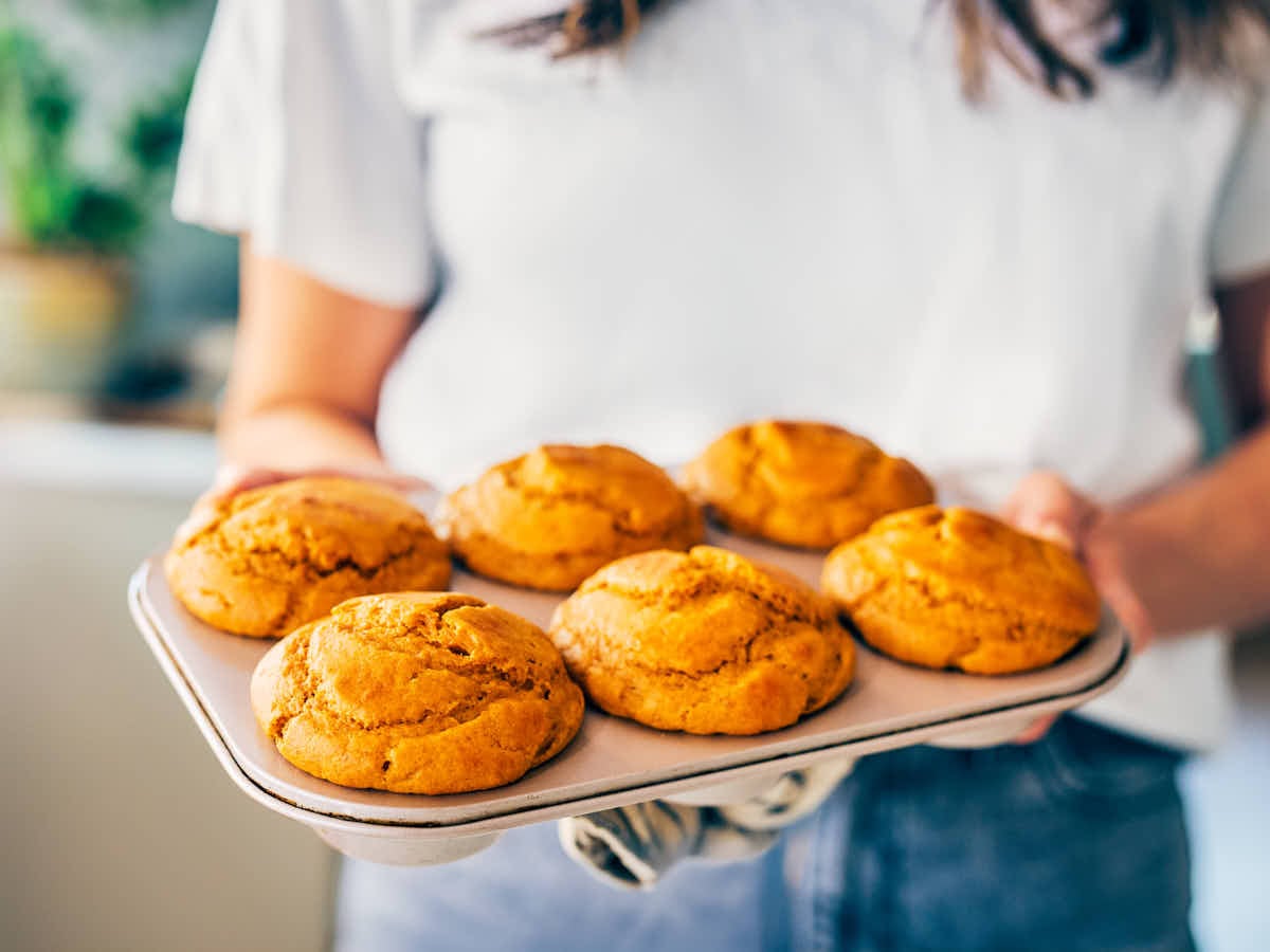 A woman holding a baking tin of pumpkin protein muffins.