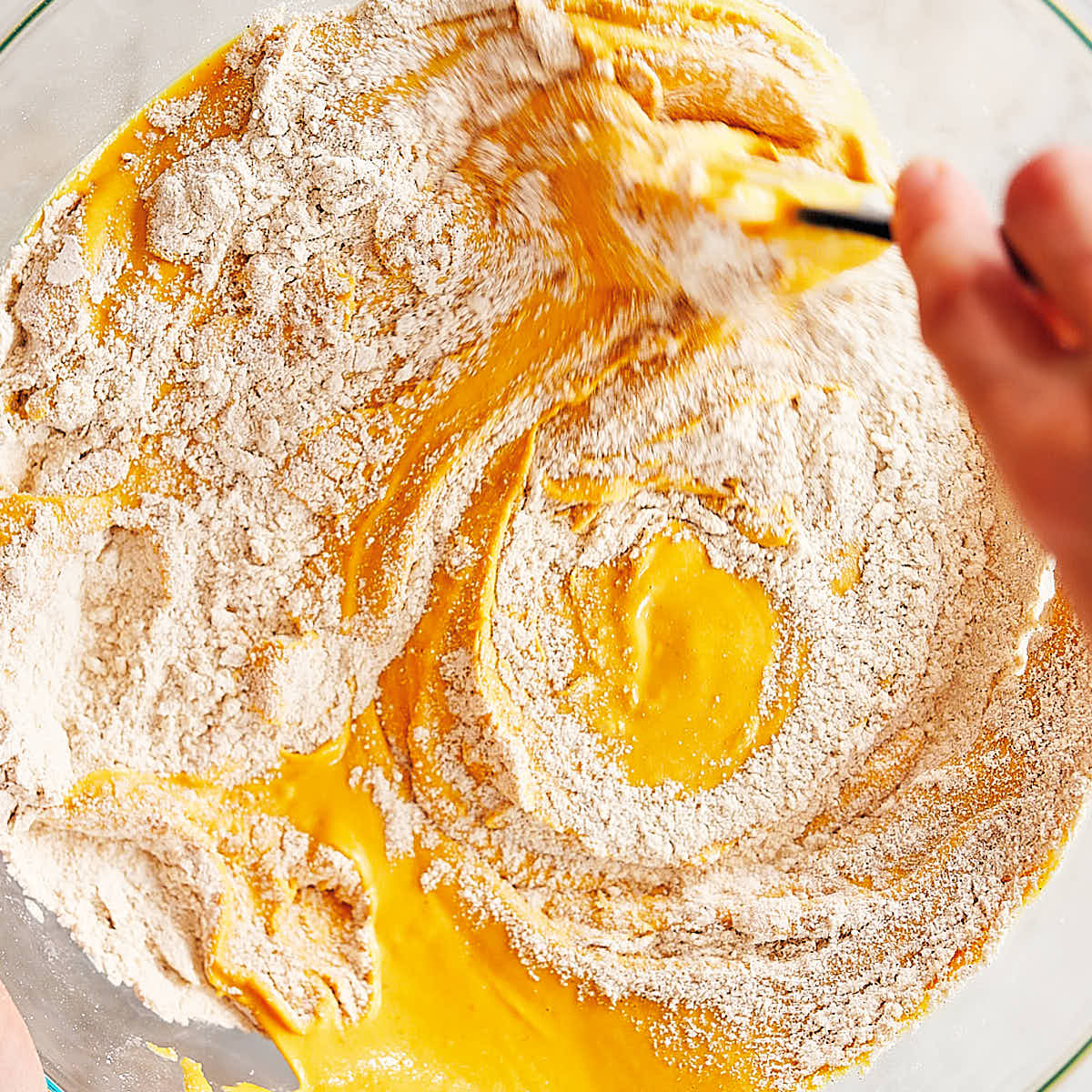 Pumpkin protein muffin batter being stirred together in a bowl.